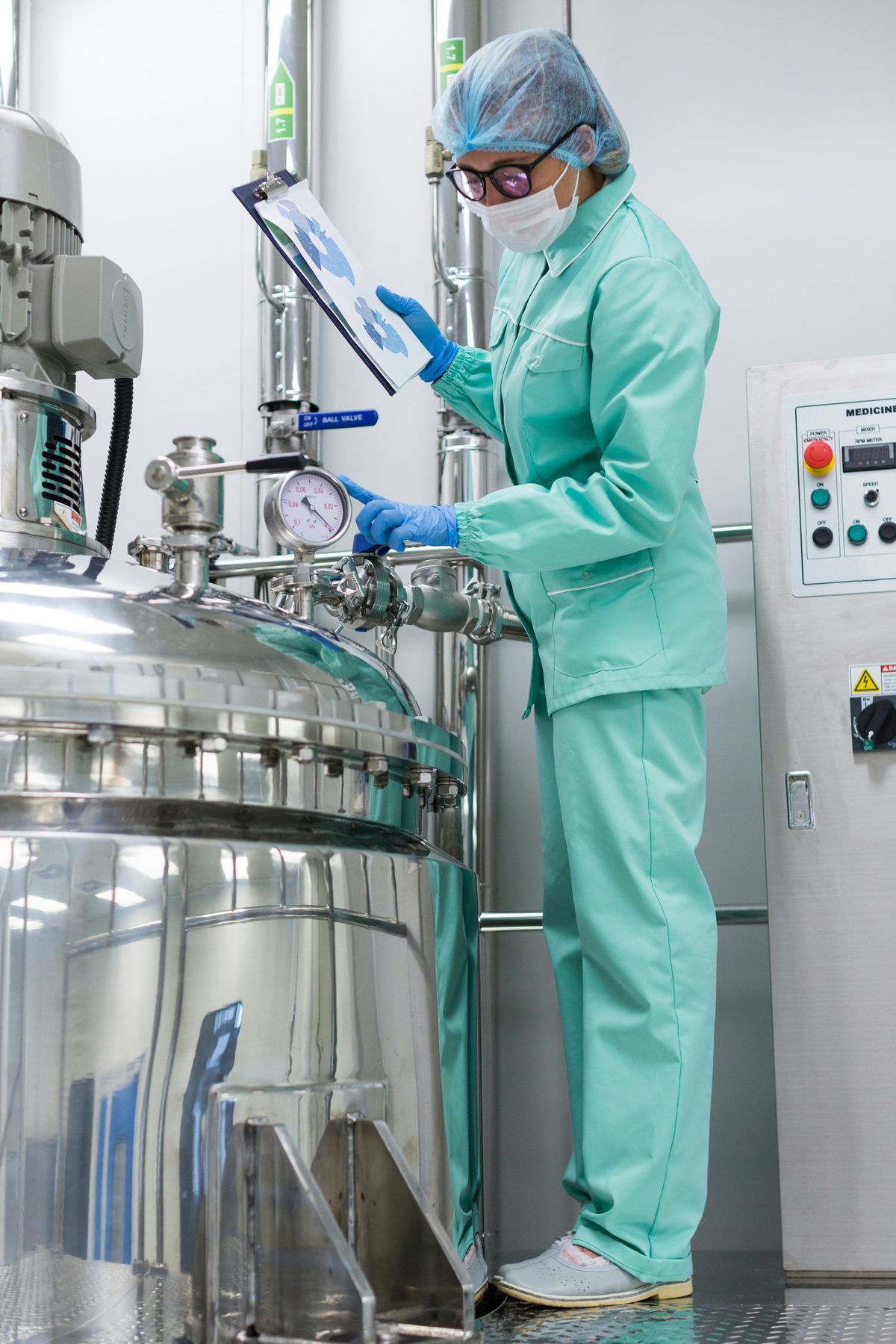 A clean-room operator in GMP conditions checking the pressure gauge of a pharmaceutical reactor